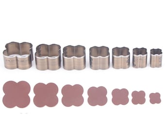 Puede incluir: Un conjunto de ocho cortadores de galletas metálicos con forma de trébol de diferentes tamaños, que van desde aproximadamente 2,5 cm hasta 6,4 cm de diámetro. Debajo, ocho piezas de material marrón con forma de trébol a juego.