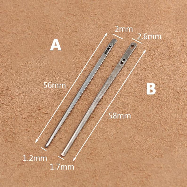 May include: Two silver leather sewing needles, labeled A and B, with measurements in millimeters. Needle A is 56 mm long and 1.2 mm wide. Needle B is 58 mm long and 1.7 mm wide. The needles have a small eye at one end and a pointed tip at the other.