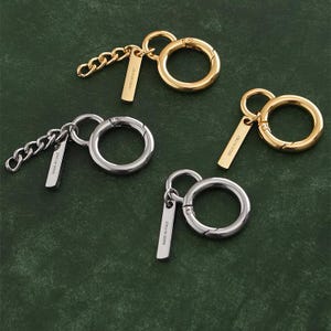 May include: Keychains in gold and silver tones, featuring a large circular clasp and a small rectangular tag. One keychain has a chain link, while the others have a simple ring. The tags read "MADE IN ITALY".