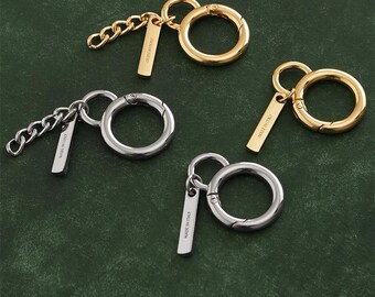 Può includere: Portachiavi in tonalità oro e argento, con un grande fermaglio circolare e una piccola etichetta rettangolare. Un portachiavi ha una catena, gli altri hanno un anello semplice. Le etichette riportano "MADE IN ITALY".