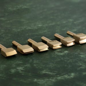 May include: Set of six leather crafting tools with different sized bevel edges. The tools are made of brass and have a polished finish. The tools are labeled with their size in millimeters: 3 mm, 4 mm, 5 mm, 6 mm, 7 mm, and 8 mm.
