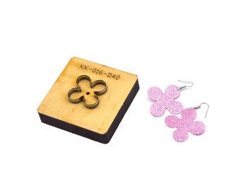 Puede incluir: Una plantilla de troquelado de madera con una forma de flor recortada. La plantilla está etiquetada como "KK-016-D40". Se muestran dos pendientes de color rosa en forma de flor junto a la plantilla.