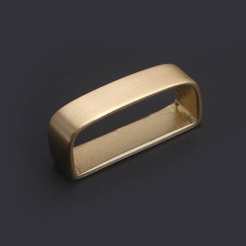 May include: A gold-toned metal belt buckle with a rectangular shape and a smooth, brushed finish.