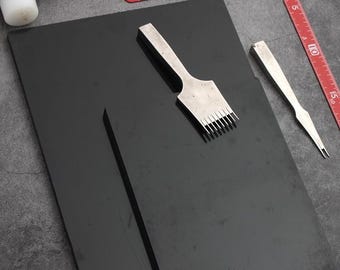 May include: A black leather working mat with a leather punch, a stitching awl, and a wooden mallet. The mat is on a gray surface.