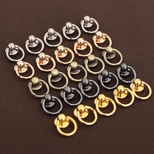 Puede incluir: Un surtido de remaches de anillo metálicos en varios acabados, incluyendo plata, oro, bronce y negro. Estos remaches presentan un diseño de anillo y son adecuados para marroquinería, fabricación de bolsos u otros proyectos de bricolaje.