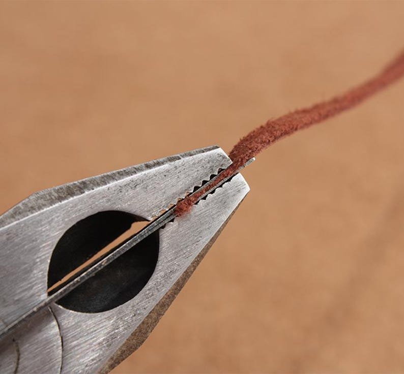 May include: Close-up of a metal tool with a serrated edge used to crimp leather cord. The cord is brown and is being held in place by the tool.