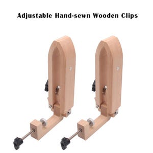 Op de afbeelding: Twee verstelbare, handgenaaide houten clips. De clips zijn gemaakt van lichtgekleurd hout en hebben een bootvormige bovenkant, een zwart verstelmechanisme en een schroef met een zwarte knop. De tekst "Adjustable Hand-sewn Wooden Clips" staat bovenaan.