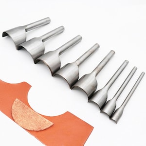 May include: Set of eight silver metal leather hole punch tools with curved edges. The tools are arranged in order of size, with the largest tool at the top and the smallest tool at the bottom.
