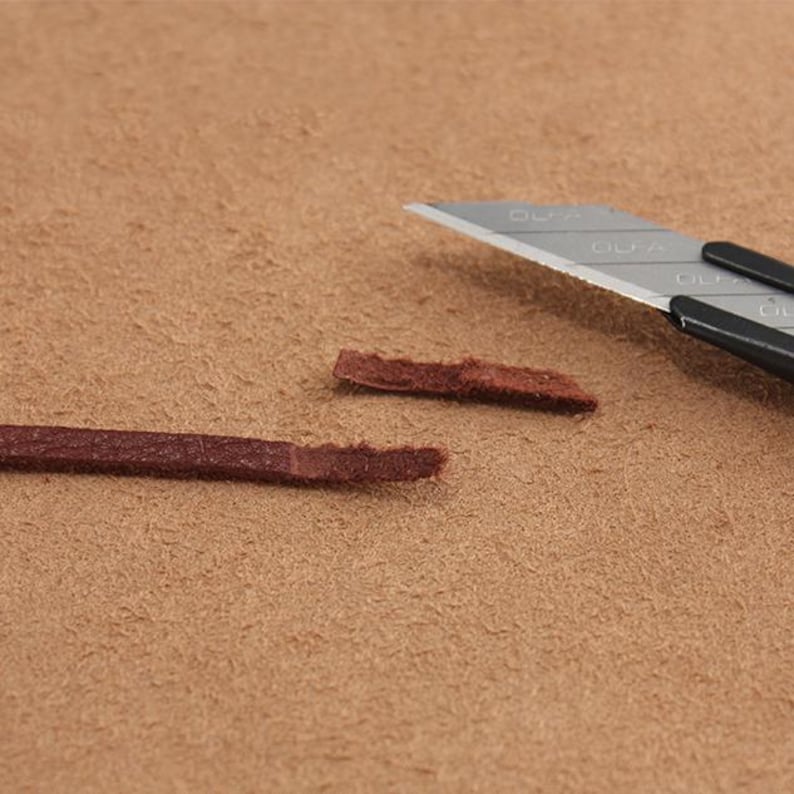 May include: Two pieces of brown leather cord have been cut with a silver utility knife. The knife has the word "OLFA" printed on it.