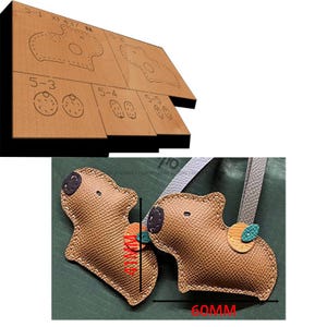 Könnte beinhalten: Zwei braune Leder-Capybara-Schlüsselanhänger mit schwarzen Augen und Nasen. Ein Schlüsselanhänger hat ein grünes und orangefarbenes Lederdetail auf der Rückseite. Die Schlüsselanhänger sind 60 mm lang.