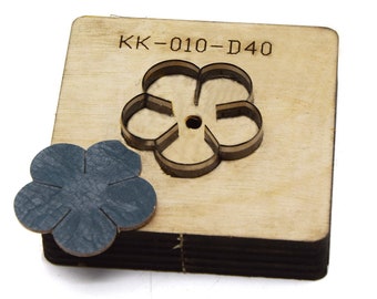Puede incluir: Un troquel de madera con una forma de flor recortada. El troquel está etiquetado como "KK-010-D40". Debajo del troquel se muestra una muestra de una flor de cuero recortada con el troquel.
