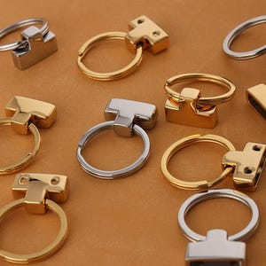 Puede incluir: Surtido de llaveros de oro y plata con un conector en forma de T. Los llaveros son de metal y tienen un acabado pulido.