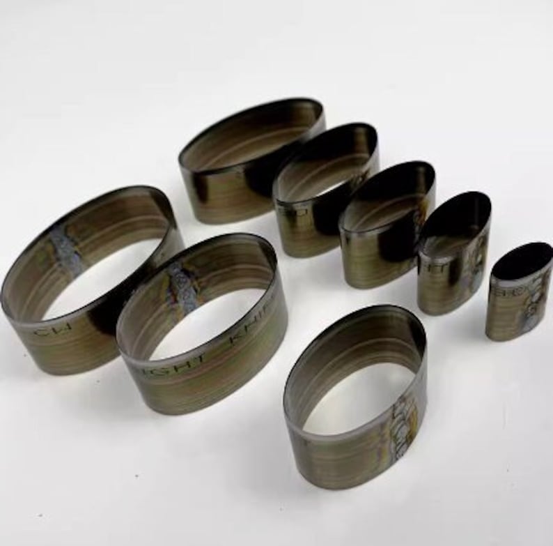 Op de afbeelding: Set van acht ovale metalen ringen, elk met een andere maat. De ringen zijn gemaakt van zilverkleurig metaal en hebben een licht getextureerd oppervlak. De ringen zijn gerangschikt in een rij van de grootste tot de kleinste.