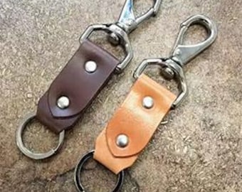 以下が含まれることがあります： 金属製の回転式クリップとキーリングが付いた革製のキーホルダー2個。1つのキーホルダーは茶色の革製、もう1つは薄い茶色の革製です。