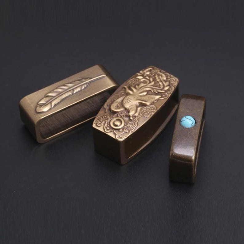 May include: Three ornate brass belt buckles with different designs. One buckle features a feather, another has a detailed floral pattern, and the third has a turquoise stone.