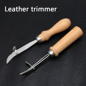 May include: Two leather trimming tools with wooden handles. The tools have a curved blade and a small screw on the top.