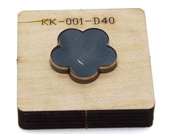Puede incluir: Un punzón artesanal de madera con un recorte en forma de flor. El punzón está etiquetado como "KK-001-D40".