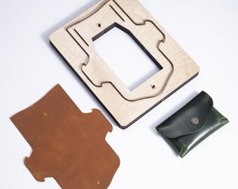 Op de afbeelding: Een leren portemonnee sjabloon met een houten snijmal en een afgewerkte groene leren portemonnee. De portemonnee heeft een klep met een decoratieve knop.