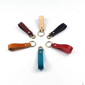 May include: Seven leather keychains in different colors, including teal, brown, red, orange, black, beige, and tan, with brass key rings.