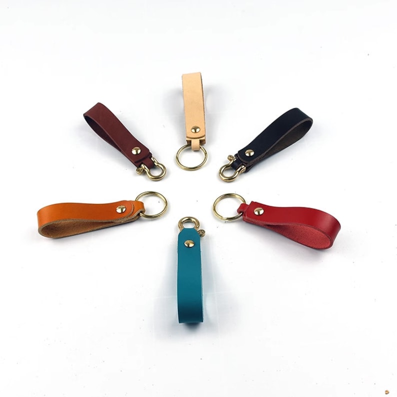 May include: Seven leather keychains in different colors, including teal, brown, red, orange, black, beige, and tan, with brass key rings.