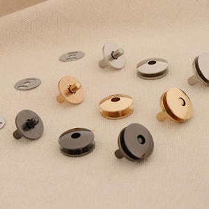 Puede incluir: Surtido de cierres magnéticos a presión en acabados plateado, dorado y negro. Los cierres están diseñados para coser en tela y están disponibles en varios tamaños.