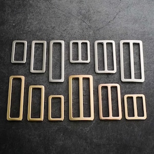 Könnte beinhalten: Sortiment an Gürtelschließen aus Metall in Silber- und Goldtönen. Die Schließen sind rechteckig mit zwei horizontalen Balken in der Mitte. Die Schließen sind in verschiedenen Größen.