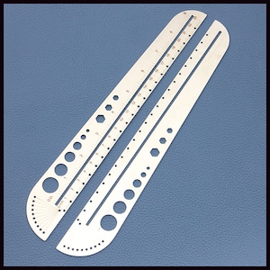 May include: A silver metal ruler with a curved edge and a series of holes and markings. The ruler has a scale in inches and centimeters.