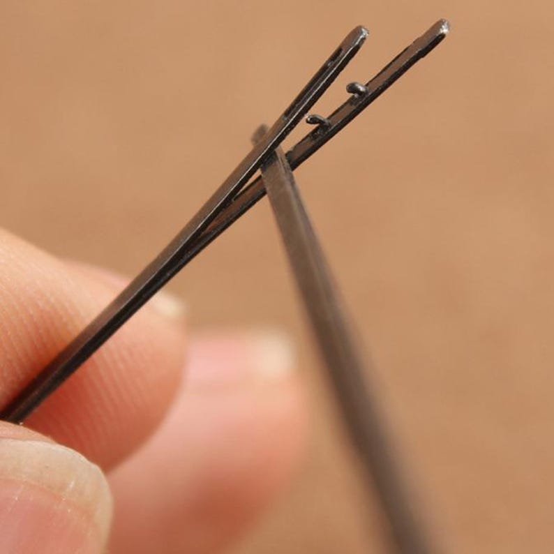 May include: Two black metal hair clips, one is open and the other is closed, showing the mechanism of the clip.