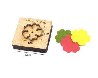 Puede incluir: Una plantilla de troquelado de madera con forma de flor, etiquetada como "KK-072-D45". La plantilla mide 4,5 cm por 4,5 cm y 8 cm de largo. Se muestran tres flores de fieltro en verde, amarillo y rojo junto a la plantilla.