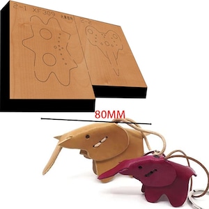 Peut inclure: Deux porte-clés en forme d'éléphant en cuir, l'un beige et l'autre bordeaux, avec un gabarit de découpe en bois pour la fabrication d'artisanat en cuir. Le gabarit est étiqueté "2-1 XF309 大物料 2-2" et mesure 80 mm.