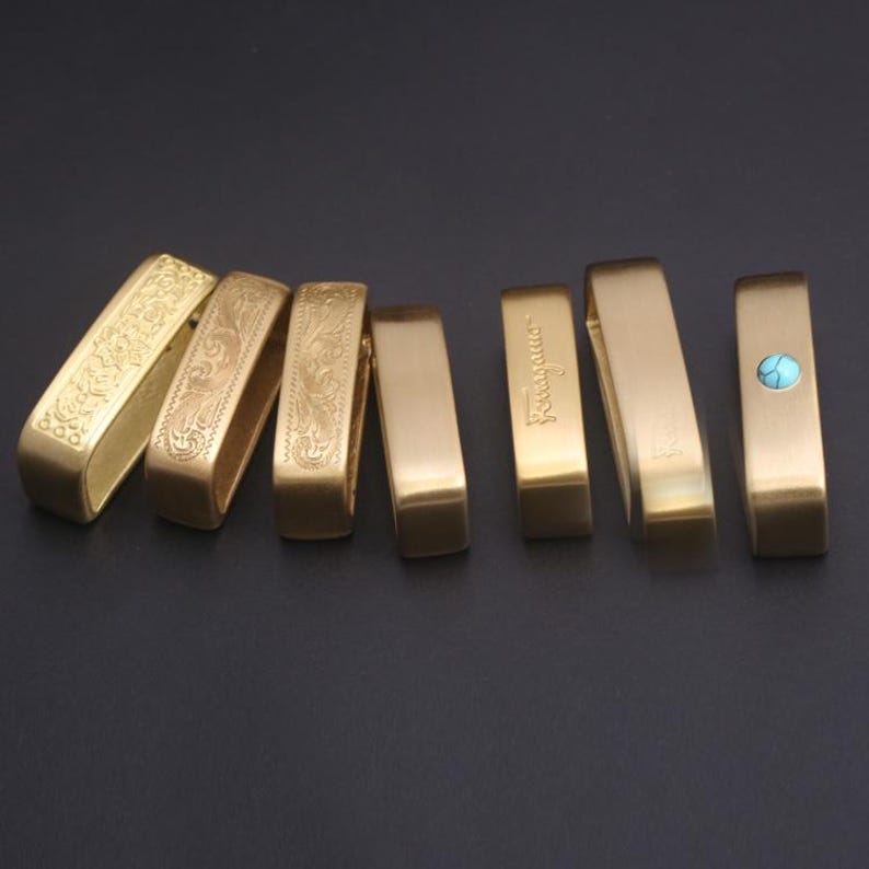 May include: Seven brass belt buckles with different designs. Some buckles have an engraved floral pattern, while others have a plain surface or a turquoise stone inlay.