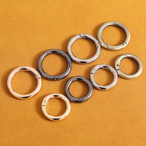 May include: Assortment of six metal key rings in various finishes, including gold, silver, and black. The rings are all closed and have a spring-loaded clasp.