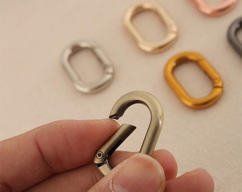 May include: A set of five metal rings in different colors and finishes. The rings are oval shaped and have a smooth surface. The rings are used for attaching to bags, keychains, or other accessories.