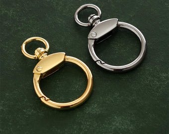 Può includere: Due portachiavi, uno dorato e uno argentato, con un anello circolare e una chiusura girevole. I portachiavi sono su uno sfondo verde.