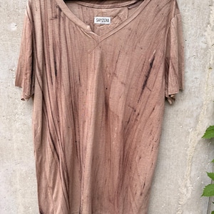 May include: A short-sleeved V-neck t-shirt in a muted tan color with dark brown vertical streaks throughout the fabric. The shirt features a white label at the inner neckline with the black text SHYZUXA printed on it, hanging on a black hanger.
