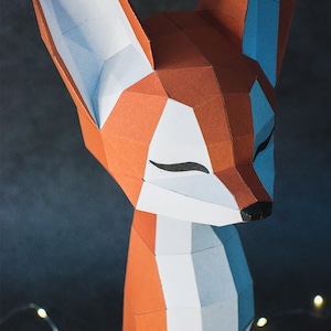 Peut inclure: Une sculpture g&eacute;om&eacute;trique en papier repr&eacute;sentant un renard, avec des accents orange, blancs et bleus. Le renard a les yeux ferm&eacute;s et un nez noir. L'&oelig;uvre est faite de papier pli&eacute; et a une esth&eacute;tique moderne et minimaliste.