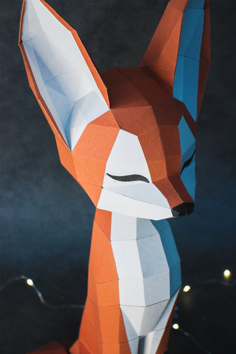Peut inclure: Une sculpture g&eacute;om&eacute;trique en papier repr&eacute;sentant un renard, avec des accents orange, blancs et bleus. Le renard a les yeux ferm&eacute;s et un nez noir. L'&oelig;uvre est faite de papier pli&eacute; et a une esth&eacute;tique moderne et minimaliste.