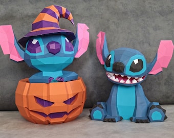 May include: Two papercraft figures of a blue alien character. One is inside an orange jack-o'-lantern, wearing a witch hat. The other is sitting, with a wide grin. Both figures have large ears and are made of geometric shapes.