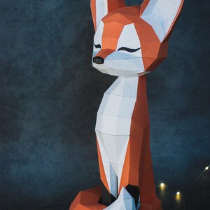 Peut inclure: Sculpture g&eacute;om&eacute;trique en papier repr&eacute;sentant un renard aux couleurs orange, blanc et noir. Le renard a un corps long et des oreilles pointues. Le renard est assis, les yeux ferm&eacute;s, ce qui lui donne une apparence paisible. Le fond est bleu fonc&eacute;.