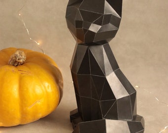 May include: A black geometric paper cat sculpture sits next to a bright orange pumpkin. The cat has a faceted design, with sharp angles and a sitting pose. The pumpkin has a textured surface and a brown stem. The background is a neutral gray.