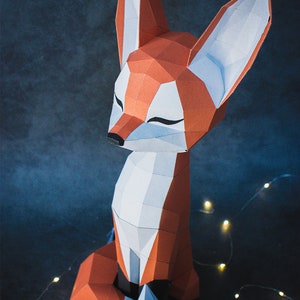 Peut inclure: Une sculpture g&eacute;om&eacute;trique en papier repr&eacute;sentant un renard, dans des tons d'orange, de blanc et de gris. Le renard est assis, les yeux ferm&eacute;s, avec un design moderne et polygonal. Le fond est bleu-gris fonc&eacute;, avec quelques petites lumi&egrave;res.