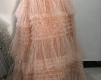 May include: A long, flowing tulle skirt with multiple layers of ruffles. The skirt is a light peach color.