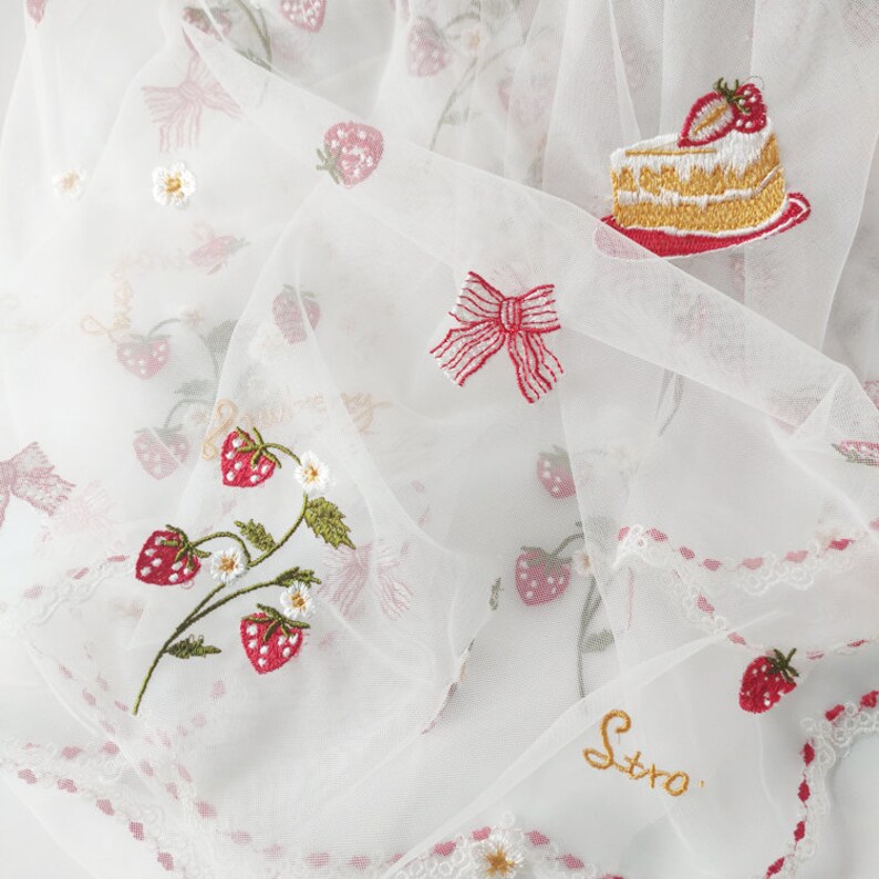 Puede incluir: Tela blanca transparente con bordados de fresas, lazos y una porci&oacute;n de pastel. La tela presenta un delicado ribete de encaje y la palabra "Stro" bordada con hilo dorado. El dise&ntilde;o incluye acentos rojos, verdes y blancos.