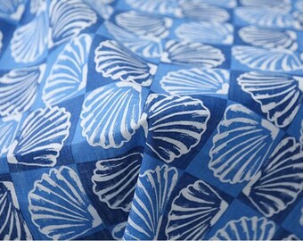 May include: Close-up of a blue fabric with a seashell pattern. The design features white seashells on a checkered background of varying shades of blue. The fabric appears to be soft and slightly wrinkled, suggesting it is a lightweight material.
