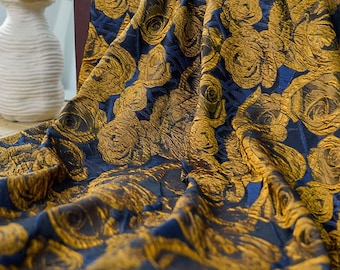 May include: A luxurious fabric with a repeating rose pattern. The fabric features a rich navy blue background with golden yellow roses. The material is draped, showcasing the texture and design. Ideal for upholstery, drapery, or fashion.