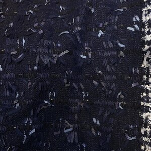 May include: Close-up of a dark blue fabric with a textured woven pattern. The fabric has a subtle sheen and is made of a variety of threads.