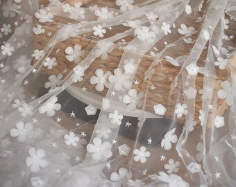 May include: White sheer fabric with a delicate floral pattern. The fabric is adorned with small white flowers and stars.