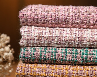 May include: A stack of five fabric swatches in different colors and textures. The swatches are pink, white, green, yellow, and black. Each swatch has a woven texture with a subtle shimmer.