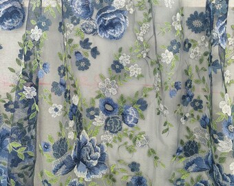 Puede incluir: Tela transparente bordada con un diseño floral. El patrón presenta flores azules grandes y pequeñas, flores blancas y hojas verdes. El tejido es semitransparente, adecuado para diversos proyectos de costura y decoración.