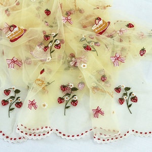 Puede incluir: Una tela transparente de color amarillo p&aacute;lido con bordados de fresas, lazos y rebanadas de pastel. La tela tiene un borde festoneado con detalles rojos en forma de coraz&oacute;n. La palabra "strawberry" est&aacute; bordada en cursiva.